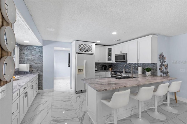 14506 Sutter Pl, Tampa, FL 33625 - kitchen with appliances with stainless steel finishes, light stone counters, glass insert cabinets, a peninsula, and light marble finish flooring