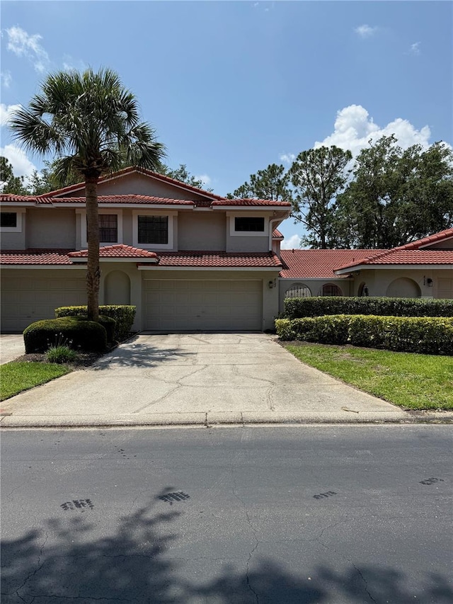mediterranean / spanish home featuring an attached garage, driveway, stucco siding, and a tile roof