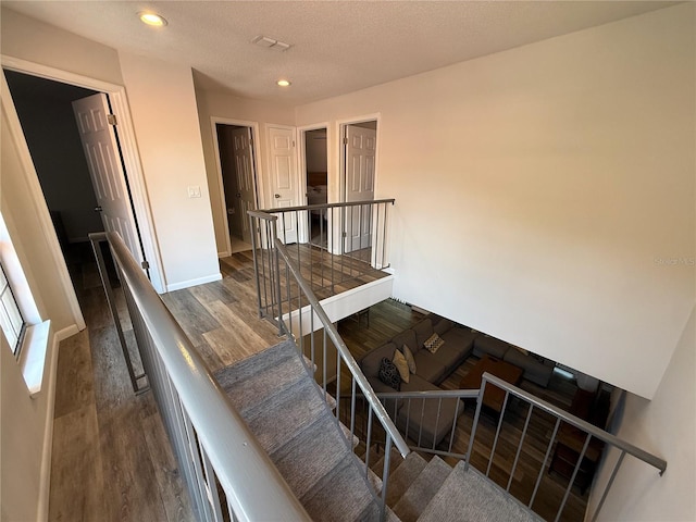 staircase featuring wood finished floors, recessed lighting, and a textured ceiling
