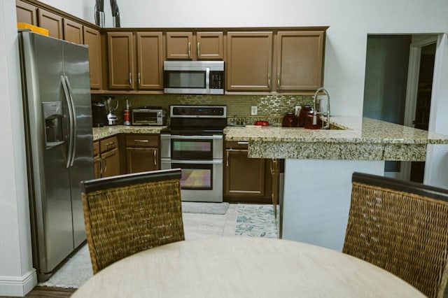 2102 Applegate Dr, Ocoee, FL 34761 - kitchen with stainless steel appliances, decorative backsplash, light stone countertops, a peninsula, and a sink