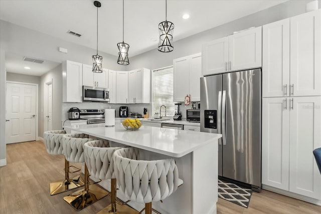 704 Honeysuckle Ave, Kissimmee, FL 34747 - kitchen with appliances with stainless steel finishes, a breakfast bar area, a kitchen island, light wood-style flooring, and white cabinets