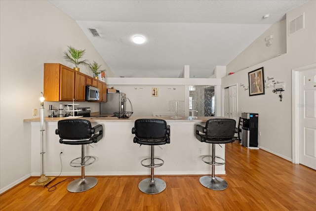 1321 Dunbarton Ct, Kissimmee, FL 34758 - kitchen with appliances with stainless steel finishes, lofted ceiling, a kitchen bar, brown cabinetry, and light wood-style floors
