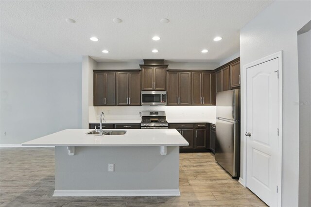 328 Cedar Bark Ln, Sanford, FL 32771 - kitchen with appliances with stainless steel finishes, a sink, dark brown cabinetry, light wood-style flooring, and a kitchen island with sink