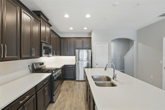 328 Cedar Bark Ln, Sanford, FL 32771 - kitchen with appliances with stainless steel finishes, a sink, light wood finished floors, arched walkways, and dark brown cabinetry