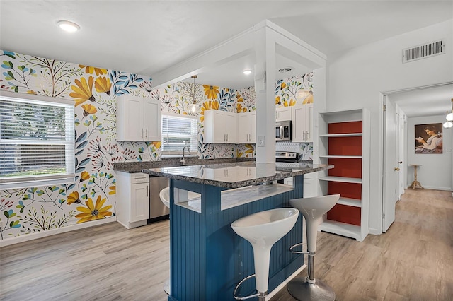 826 Cherokee Cir, Sanford, FL 32773 - kitchen featuring wallpapered walls, stainless steel microwave, a kitchen breakfast bar, white cabinets, and light wood finished floors