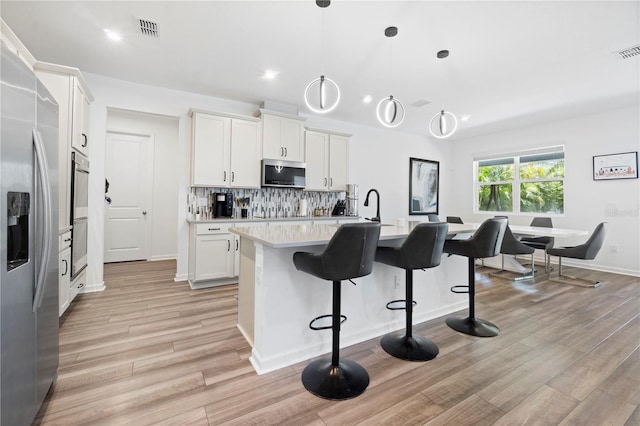 2227 Blue Salvia St, Clermont, FL 34711 - kitchen featuring stainless steel appliances, light countertops, light wood-style floors, and a breakfast bar area