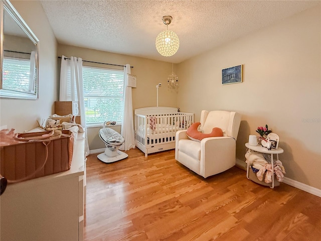 6047 Shore Line Dr, Orlando, FL 32819 - bedroom with light wood-type flooring, a textured ceiling, a crib, baseboards, and a chandelier