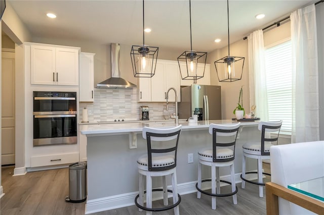 12259 Bracco St, Winter Garden, FL 34787 - kitchen with wall chimney range hood, double oven, stainless steel fridge, wood finished floors, and light countertops