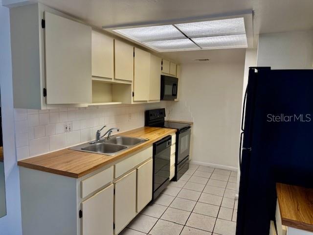 5269 Vineland Rd Unit 101, Orlando, FL 32811 - kitchen featuring black appliances, a sink, light tile patterned flooring, decorative backsplash, and baseboards