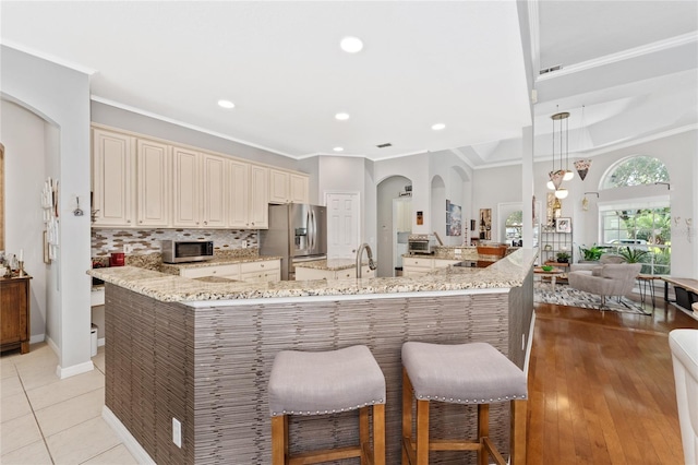 13108 Lakeshore Grove Dr, Winter Garden, FL 34787 - kitchen with cream cabinetry, appliances with stainless steel finishes, arched walkways, a kitchen breakfast bar, and light stone counters