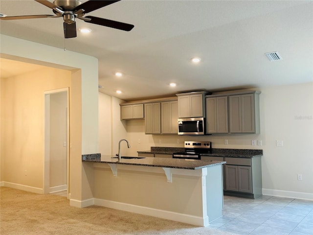 4326 Sagefield Dr, Harmony, FL 34773 - kitchen featuring appliances with stainless steel finishes, gray cabinets, a sink, a breakfast bar, and dark stone countertops