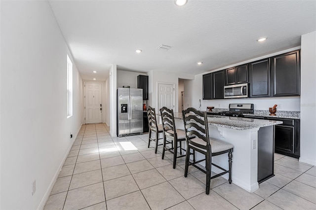 29400 Caspian St, Leesburg, FL 34748 - kitchen featuring appliances with stainless steel finishes, dark cabinets, light tile patterned floors, a breakfast bar area, and a kitchen island with sink