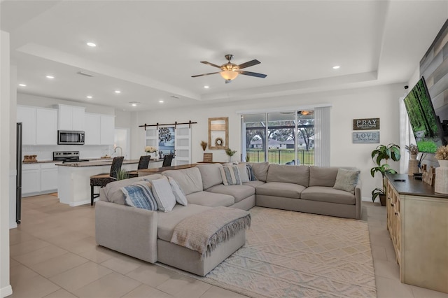 10815 Laxer Cay Loop, San Antonio, FL 33576 - living room featuring a tray ceiling, a ceiling fan, a barn door, light tile patterned flooring, and recessed lighting