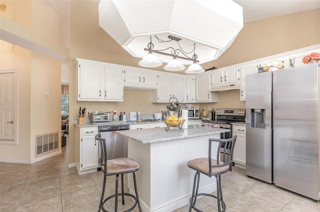 1910 Palm View Dr, Apopka, FL 32712 - kitchen featuring appliances with stainless steel finishes, under cabinet range hood, light tile patterned flooring, white cabinets, and vaulted ceiling