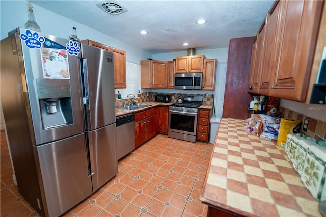 kitchen featuring stainless steel appliances, a sink, brown cabinets, recessed lighting, and a textured ceiling