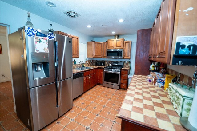 kitchen featuring stainless steel appliances, brown cabinets, recessed lighting, a sink, and a textured ceiling