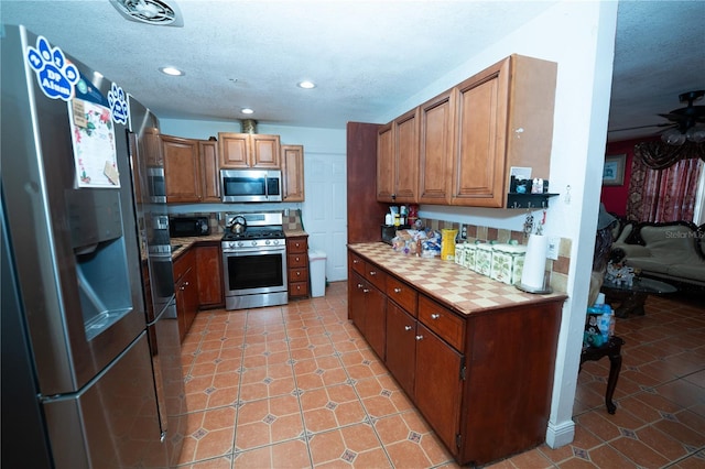 kitchen with appliances with stainless steel finishes, brown cabinets, recessed lighting, light tile patterned floors, and a textured ceiling