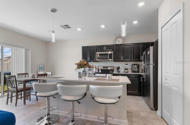 601 Watusi Way, Saint Cloud, FL 34772 - kitchen featuring stainless steel appliances, light countertops, dark cabinetry, a kitchen island with sink, and a kitchen breakfast bar