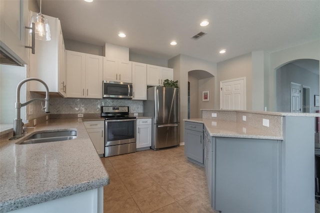 3223 Blazing Star Ln, Harmony, FL 34773 - kitchen featuring appliances with stainless steel finishes, a sink, arched walkways, a kitchen island, and decorative backsplash
