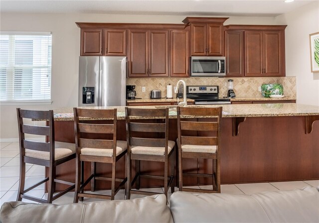 1836 Sandy Park Trl, Kissimmee, FL 34747 - kitchen featuring stainless steel appliances, light tile patterned floors, backsplash, light stone countertops, and a kitchen bar