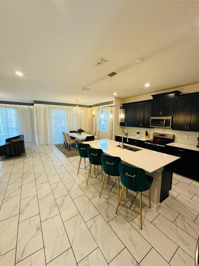851 Drop Shot Dr, Davenport, FL 33896 - kitchen featuring appliances with stainless steel finishes, a sink, dark cabinetry, light marble finish floors, and a breakfast bar area