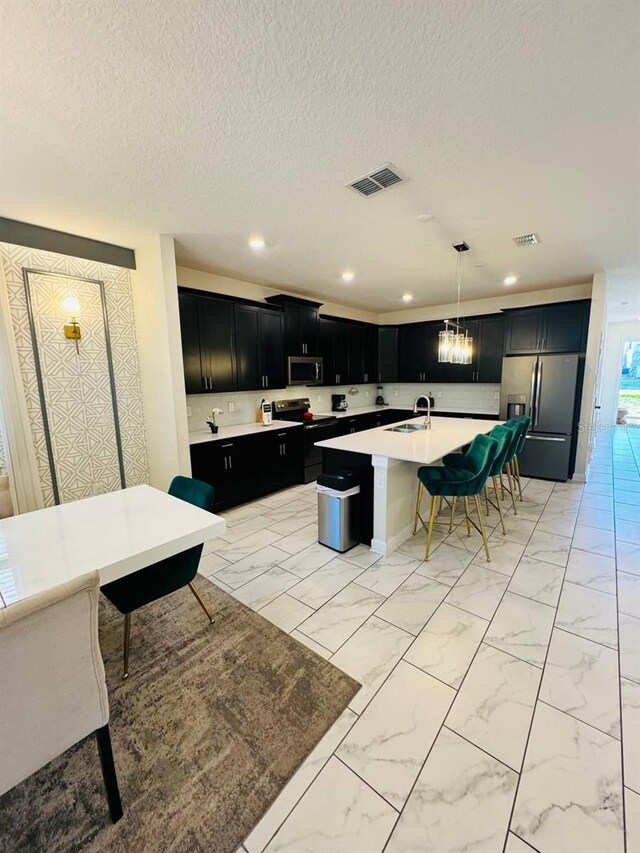 851 Drop Shot Dr, Davenport, FL 33896 - kitchen with appliances with stainless steel finishes, dark cabinetry, a sink, light countertops, and a center island with sink