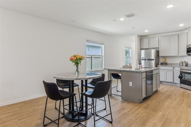 4122 Sagefield Dr, Saint Cloud, FL 34773 - kitchen featuring appliances with stainless steel finishes, light wood-style flooring, a kitchen island with sink, light stone countertops, and a sink