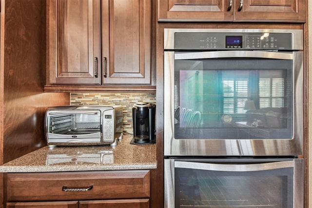4133 Foxhound Dr, Clermont, FL 34711 - kitchen with stainless steel double oven, backsplash, and light stone counters