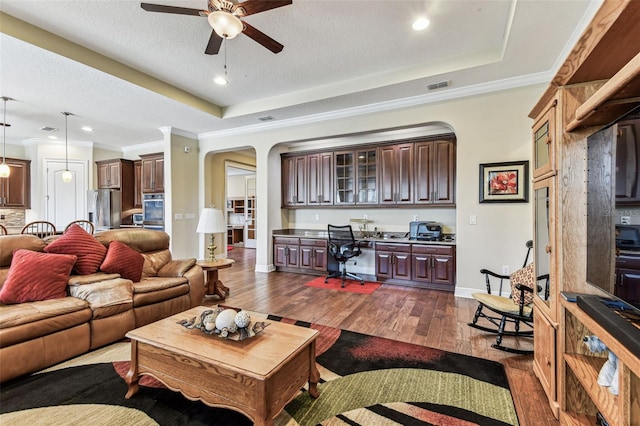 4133 Foxhound Dr, Clermont, FL 34711 - living room with arched walkways, a ceiling fan, a tray ceiling, dark wood-style floors, and crown molding