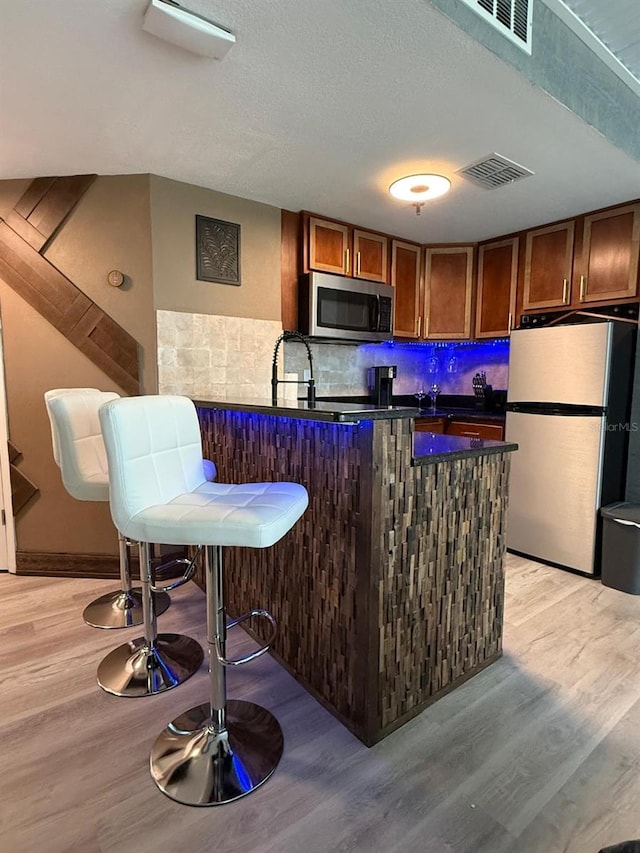 6165 Carrier Dr Unit 1801, Orlando, FL 32819 - kitchen featuring stainless steel appliances, dark countertops, light wood finished floors, a peninsula, and decorative backsplash