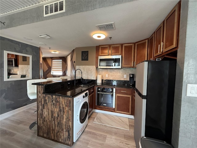 6165 Carrier Dr Unit 1801, Orlando, FL 32819 - kitchen with appliances with stainless steel finishes, washer / dryer, light wood finished floors, and a peninsula