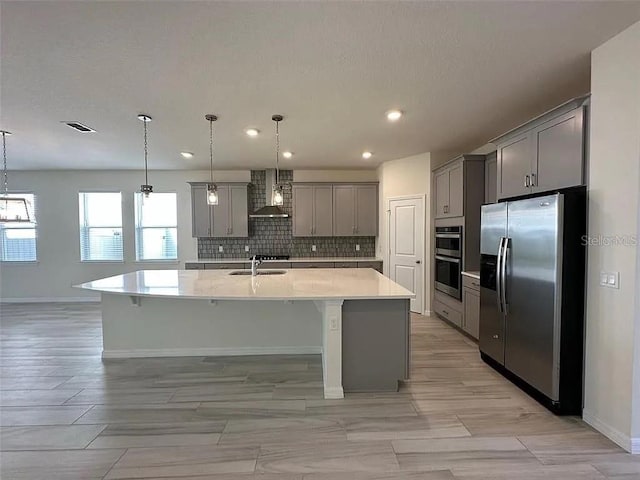 605 Big Pine Ave, Minneola, FL 34715 - kitchen featuring stainless steel appliances, gray cabinets, wall chimney exhaust hood, light countertops, and a large island