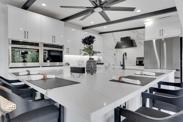 1700 Lake Markham Rd, Sanford, FL 32771 - kitchen with stainless steel appliances, wall chimney range hood, white cabinetry, beam ceiling, and decorative backsplash