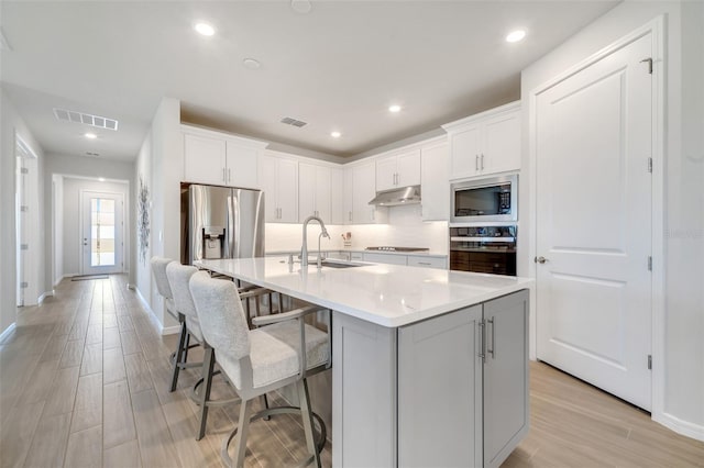 2479 Pine Preserve Ct, Saint Cloud, FL 34771 - kitchen featuring appliances with stainless steel finishes, under cabinet range hood, a sink, decorative backsplash, and an island with sink