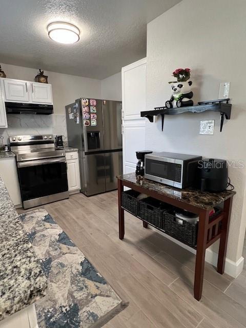 1620 Hialeah St, Orlando, FL 32808 - kitchen featuring stainless steel appliances, ventilation hood, white cabinets, light wood-type flooring, and a textured ceiling