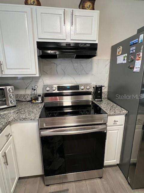 1620 Hialeah St, Orlando, FL 32808 - kitchen featuring appliances with stainless steel finishes, under cabinet range hood, white cabinets, light wood-type flooring, and tasteful backsplash