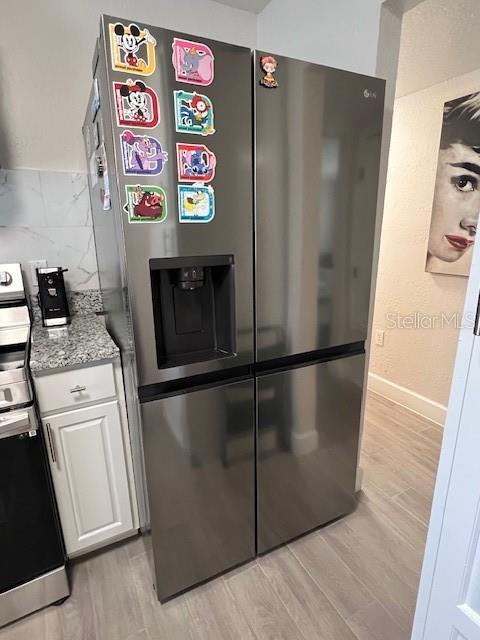 1620 Hialeah St, Orlando, FL 32808 - kitchen with stainless steel appliances, white cabinets, light wood finished floors, light stone countertops, and baseboards