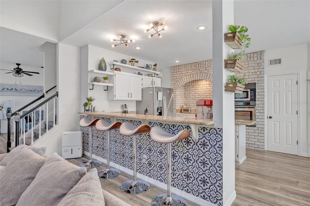 9455 Belmont Ter, Oviedo, FL 32765 - kitchen featuring appliances with stainless steel finishes, open shelves, light wood-style flooring, ceiling fan, and a kitchen breakfast bar
