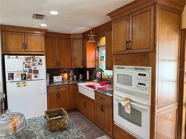 11314 Huggins St, Leesburg, FL 34788 - kitchen with white appliances, a sink, brown cabinets, decorative backsplash, and dark stone counters