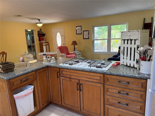 11314 Huggins St, Leesburg, FL 34788 - kitchen featuring white gas cooktop, brown cabinetry, dark stone countertops, light tile patterned flooring, and open floor plan