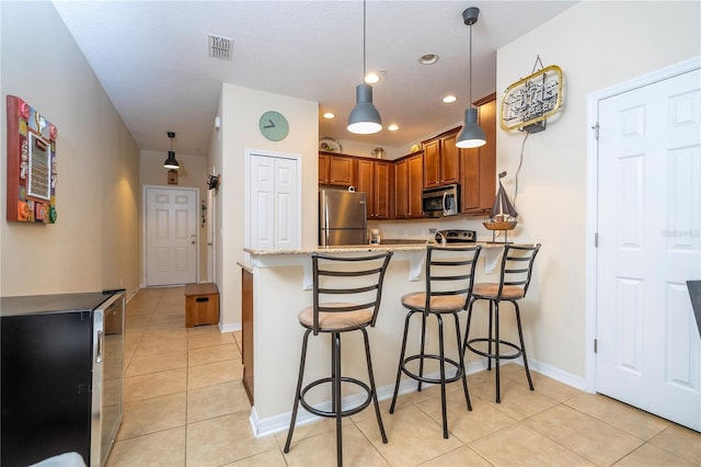 14231 Desert Haven St Unit Ge, Windermere, FL 34786 - kitchen featuring stainless steel appliances, a peninsula, brown cabinetry, light tile patterned flooring, and a breakfast bar