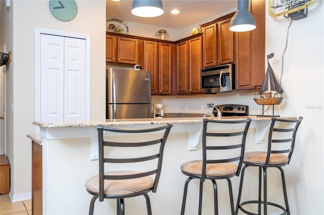 14231 Desert Haven St Unit Ge, Windermere, FL 34786 - kitchen with stainless steel appliances, a breakfast bar area, brown cabinets, light stone countertops, and light tile patterned flooring