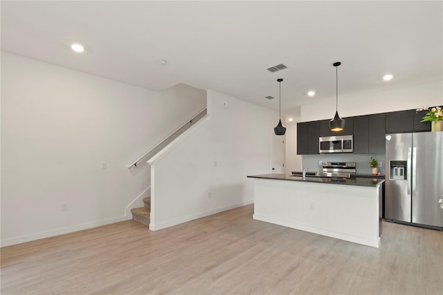 3301 Tranquil Trl, Kissimmee, FL 34747 - kitchen featuring appliances with stainless steel finishes, dark cabinets, dark countertops, light wood finished floors, and decorative backsplash