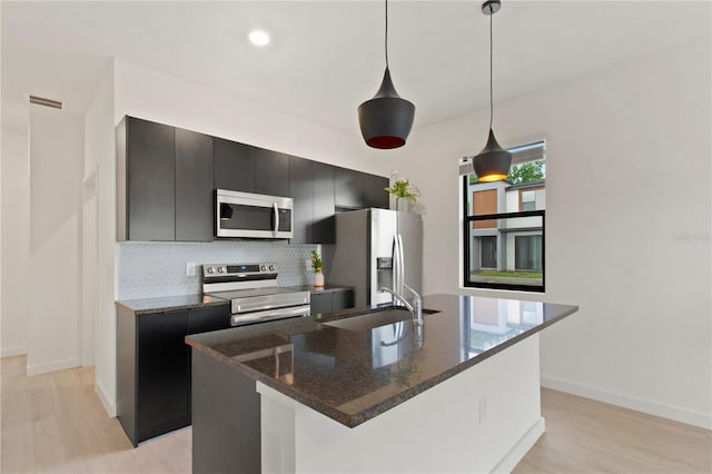 3301 Tranquil Trl, Kissimmee, FL 34747 - kitchen featuring stainless steel appliances, dark cabinetry, light wood-style floors, and decorative backsplash