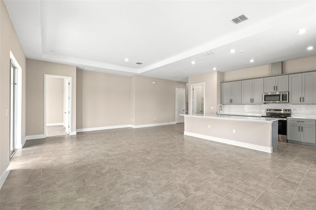 1262 Champions Dr, Daytona Beach, FL 32124 - kitchen featuring appliances with stainless steel finishes, gray cabinetry, a kitchen island with sink, light countertops, and decorative backsplash