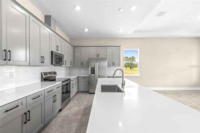 1262 Champions Dr, Daytona Beach, FL 32124 - kitchen featuring stainless steel appliances, a sink, gray cabinetry, decorative backsplash, and light countertops