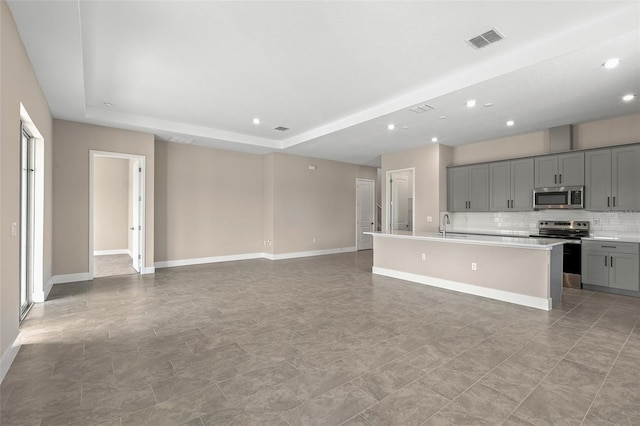 1262 Champions Dr, Daytona Beach, FL 32124 - kitchen with appliances with stainless steel finishes, gray cabinets, tasteful backsplash, a kitchen island with sink, and light countertops