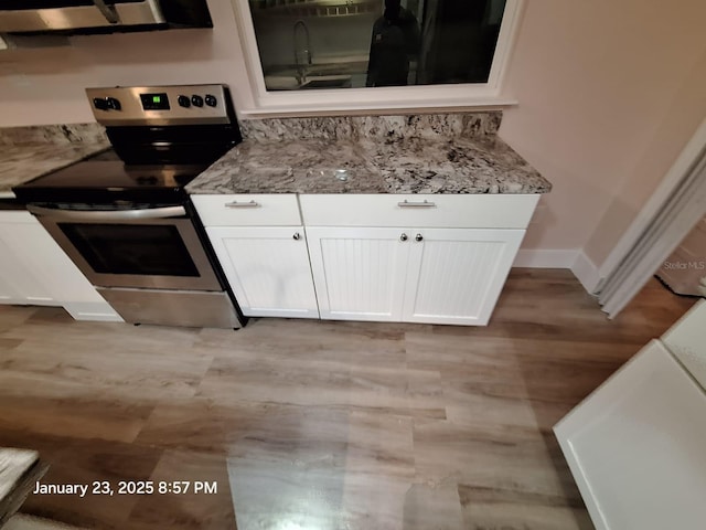 6505 Oelsner St, New Port Richey, FL 34652 - kitchen with stainless steel electric stove, white cabinetry, light stone countertops, and baseboards