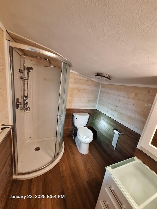 6505 Oelsner St, New Port Richey, FL 34652 - bathroom featuring a textured ceiling, wooden walls, a stall shower, toilet, and wood finished floors