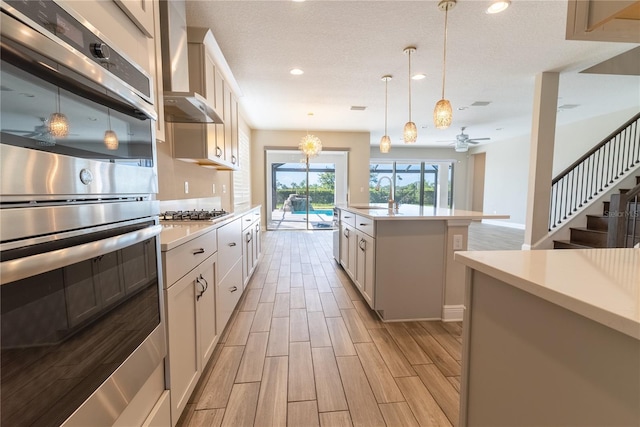 4861 Antrim Dr, Sarasota, FL 34240 - kitchen featuring appliances with stainless steel finishes, light countertops, wall chimney range hood, light wood-style flooring, and pendant lighting